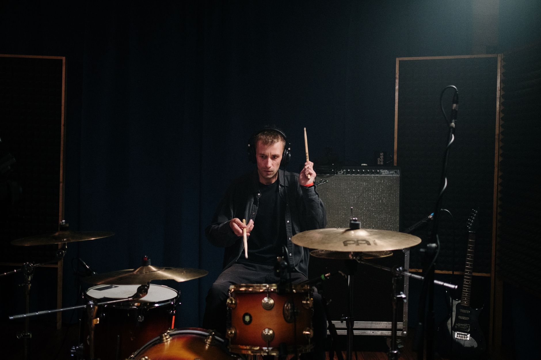 Batteur portant un casque, baguettes en main, dans un studio faiblement éclairé.